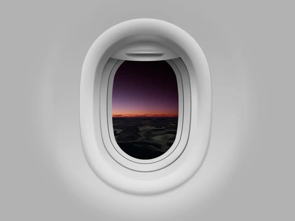 View through an airplane window over a dark landscape at sunset, with a purple sky and orange horizon.
