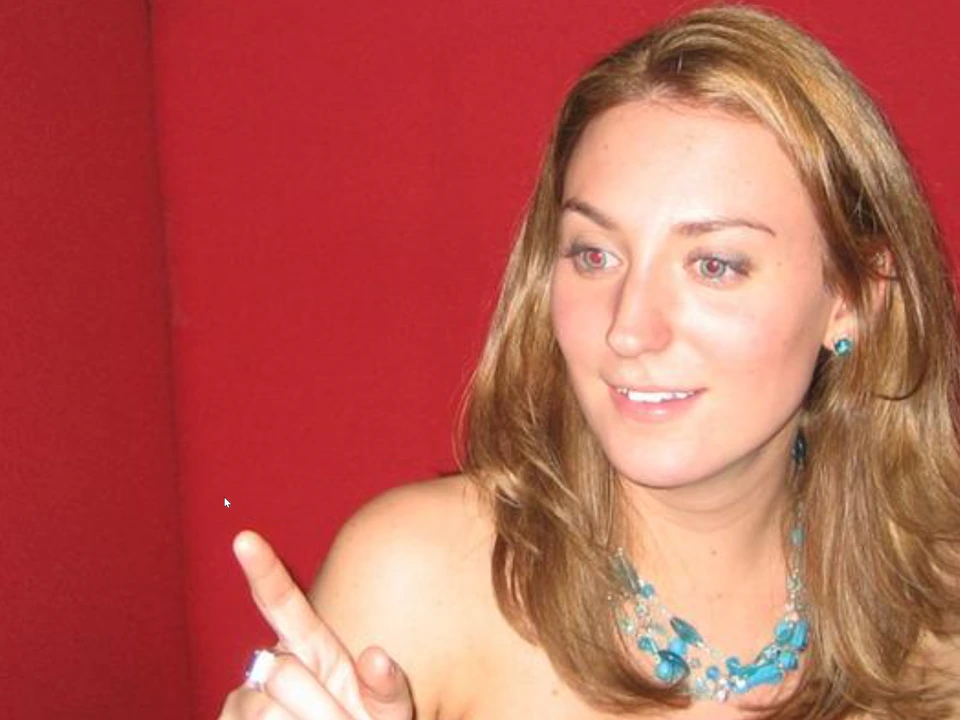 Woman with long light-brown hair and a turquoise necklace pointing toward the mouse cursor against a red background.